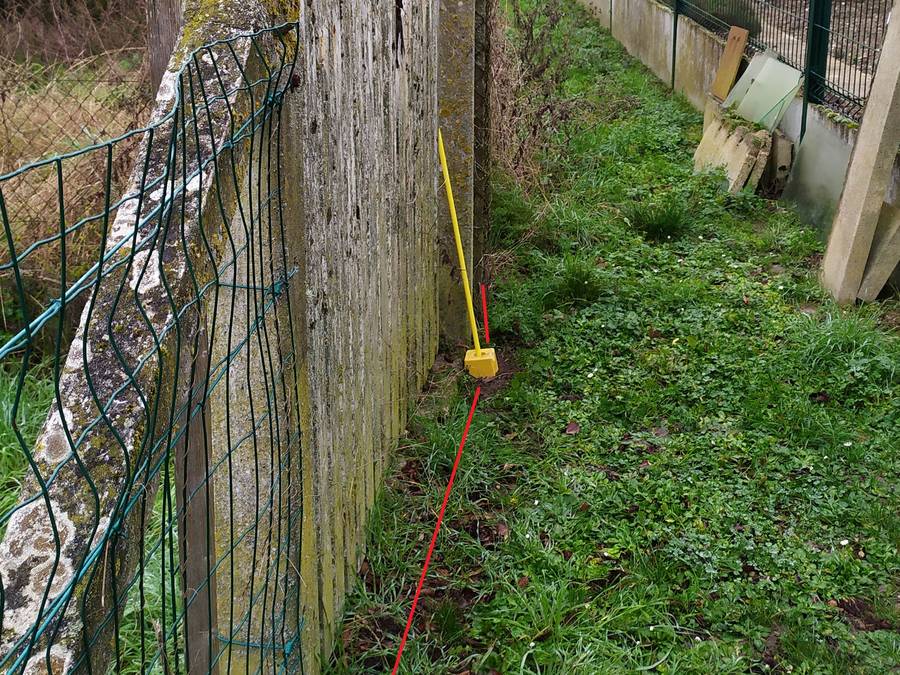 Jalon jaune et trait rouge de limite le long d'une palissade ancienne, entre deux clôtures qui ne coïncident pas